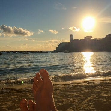 Nakne føtter på en strand-bukt i solnedgang